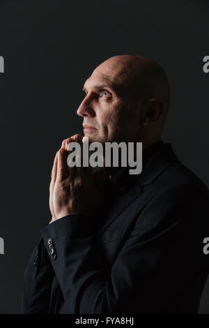 Handsome peaceful man in dark suit praying over black background Stock Photo