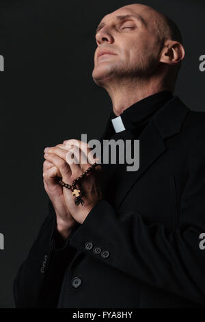 Priest standing with eyes closed and praying over black background Stock Photo