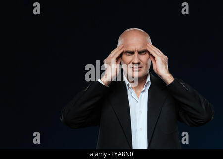 Mature businessman with headache standing over black background Stock Photo