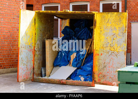 Metal container with open doors showing some trash and debris. Container is full of dry red, and yellow paint. Stock Photo