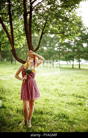 Beautiful Young Red Hair Woman in Light Dress Standing near Tree in Park. Summer Evening. Stock Photo