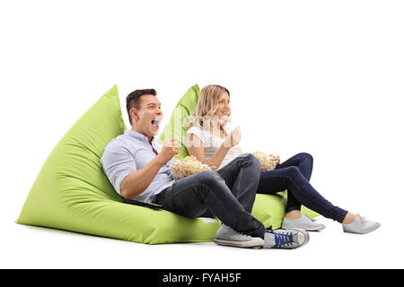 Joyful man and woman eating popcorn seated on beanbags and watching something isolated on white background Stock Photo