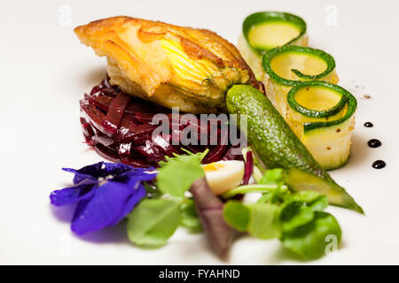 Delicious gourmet plate featuring biscuit sandwich with beets, zucchini strips and pansy garnish over white background Stock Photo