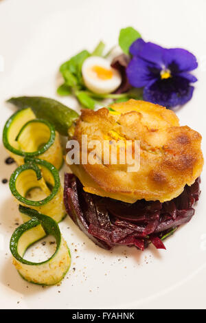 Delicious gourmet plate featuring biscuit sandwich with beets, zucchini strips and pansy garnish over white background Stock Photo