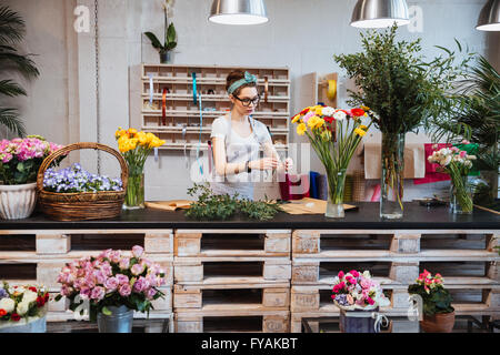 Cute concentrated young female florist in glasses working in flower shop Stock Photo