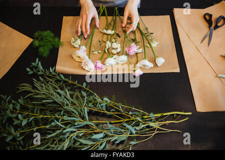 Top view of hands of female florist arranging flowers for making bouquet on black table Stock Photo