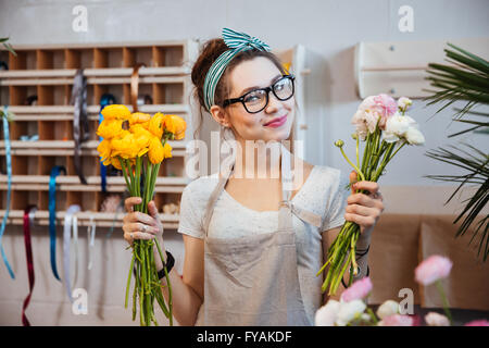 Happy beautiful young woman florist holding white and yellow flowers in shop Stock Photo