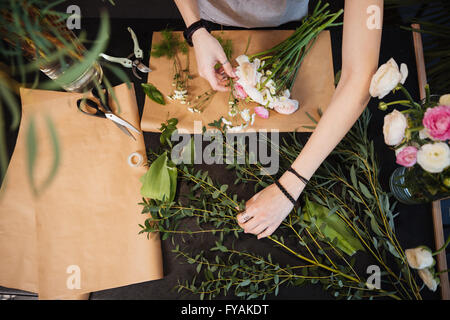 Top view of hands of young woman florist creating bouquet of flowers on black table Stock Photo
