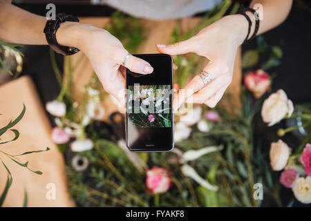 Top view of hands of woman florist taking pictures of flowers with mobile phone