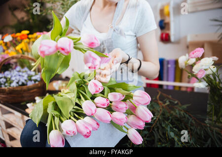 Closeup of young woman florist sitting and taking care of pink tulips in flower shop Stock Photo