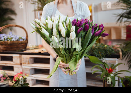 Closeup of young woman florist standing and holding bouquet of tulips in flower shop Stock Photo