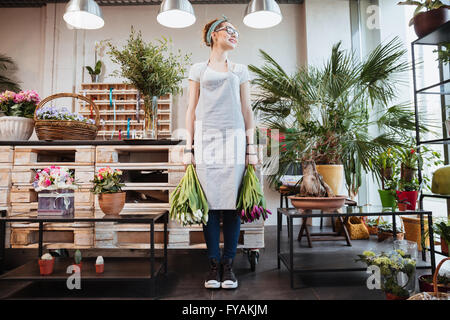 Smiling pretty young woman florist with two bunches of tulips standing in flower shop Stock Photo