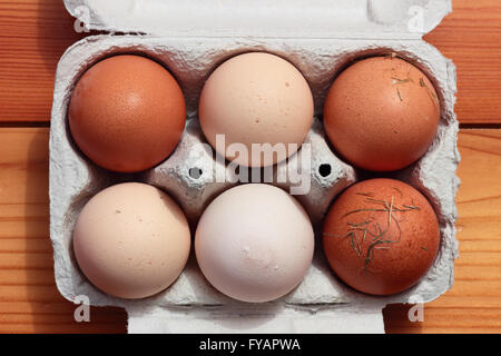 Top view of six fresh farm eggs with straw bits in an open cardboard carton on a rustic wooden background Stock Photo