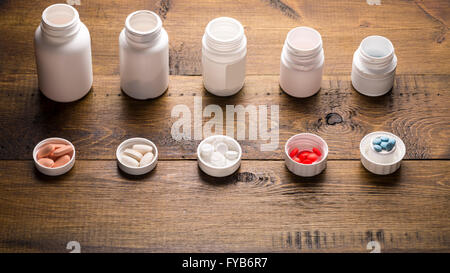 Line of medical bottles with different colored pills on dark wooden background Stock Photo