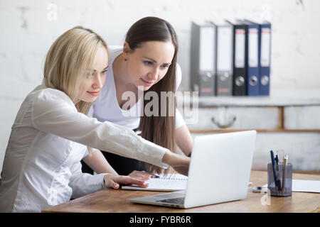 Group portrait of two beautiful smiling young office women looking at laptop screen on office desk Stock Photo
