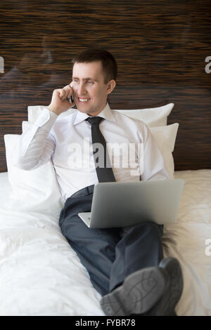 Handsome cheerful young business man sitting with laptop and talking on phone. Businessman working at home or in trip Stock Photo