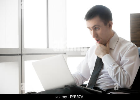 Handsome young businessman sitting in his office using laptop. Caucasian business man in formal wear looking at computer screen Stock Photo