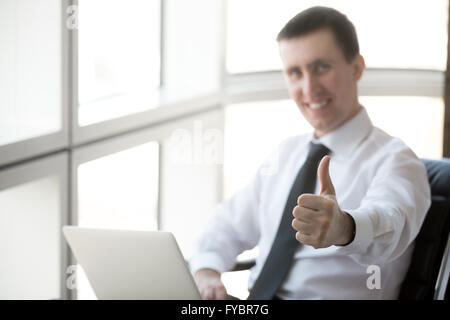 Portrait of cheerful handsome young business man sitting in his office and working on laptop computer. Happy businessperson Stock Photo