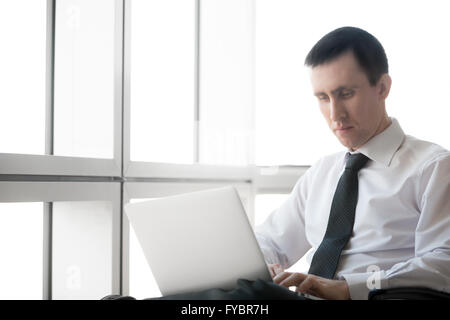 Portrait of serious handsome young business man working on laptop computer. Caucasian businessperson in formal wear during Stock Photo