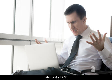 Handsome young stressed businessman sitting in his office using laptop. Caucasian businessperson looking at screen Stock Photo