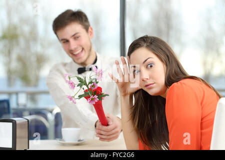 Disgusted woman rejecting a geek boy offering flowers in a blind date in a coffee shop interior Stock Photo