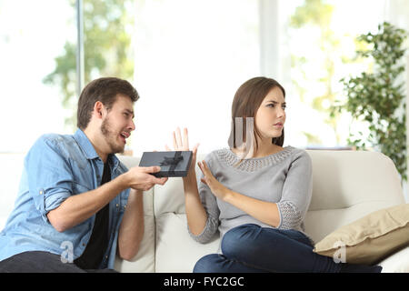 Angry girlfriend rejecting a gift sitting on a couch at home. Couple problems concept Stock Photo