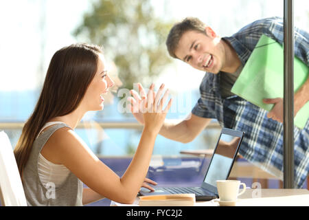 Happy friends or couple greeting waving hands and looking each other in a date in a coffee shop Stock Photo