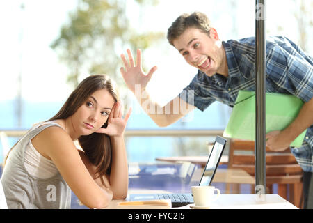Girl ignoring and rejecting to a stalker man waving her in a coffee shop in a blind date Stock Photo
