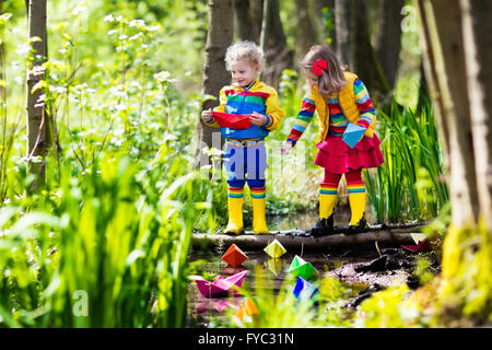 Children play with colorful paper boats in a small river on a sunny spring day. Kids playing exploring the nature. Stock Photo