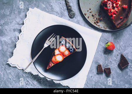 Slice of chocolate mousse tart (pie) topped with strawberries, blueberries and cranberries on black plate. Table top view Stock Photo