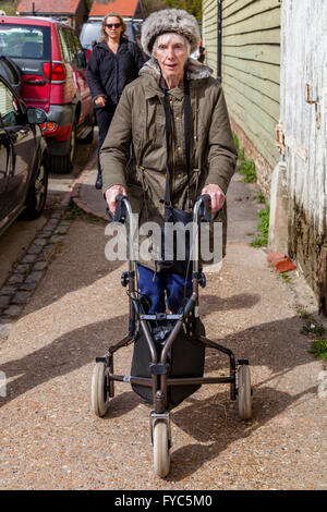 A Female Relative Watches An Disabled Elderly Woman Using A Three Wheel Rollator, Sussex, UK Stock Photo