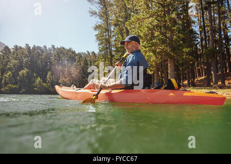 Portrait of a mature man with kayak in a lake. Senior man paddling kayak on a summer day. Stock Photo