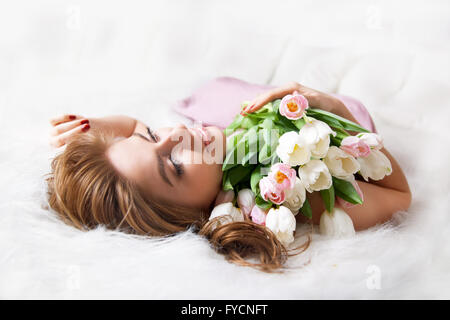 Young woman with a bouquet of flowers on the bed. Stock Photo