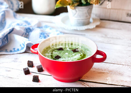 Spinach soup with croutons in red bowl on wooden table Stock Photo