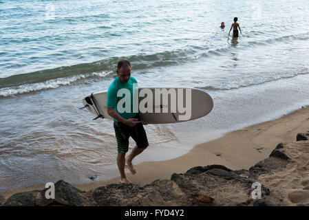 A surfer walks out of the sea at a beach in Sri Lanka Stock Photo