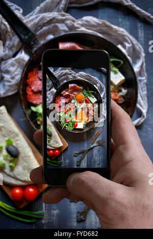 Man photographing served fried eggs with cheese and meat in the pan on wooden background Stock Photo