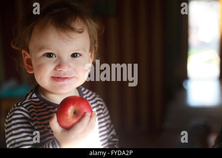 A 15 months young boy enjoys red apple for breakfast, looks into the lense Stock Photo