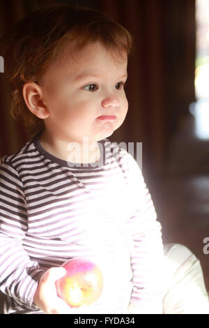 A 15 months young child enjoys apple for breakfast and a spring sun. Apple a day keeps doctors away Stock Photo
