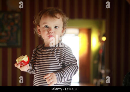 A 15 months kid enjoys fresh apple and watches with curiosity Stock Photo