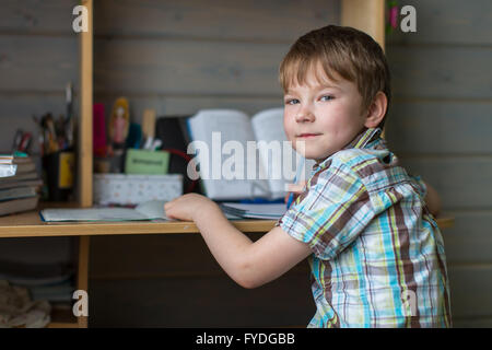 Boy sitting at table doing homework. Looking at the camera. Stock Photo