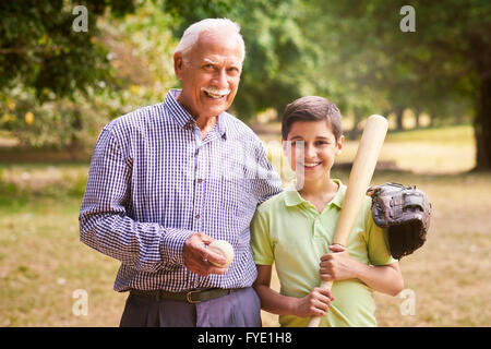 Grandpa spending time with grandson: Portrait of senior man playing baseball with his grandchild in park. The old man embraces t Stock Photo