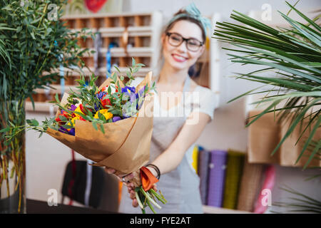 Happy charming young woman florist giving bouquet of colorful flowers to you Stock Photo
