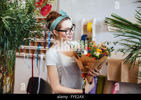 Smiling attractive young woman florist standing and holding bouquet of flowers in shop Stock Photo