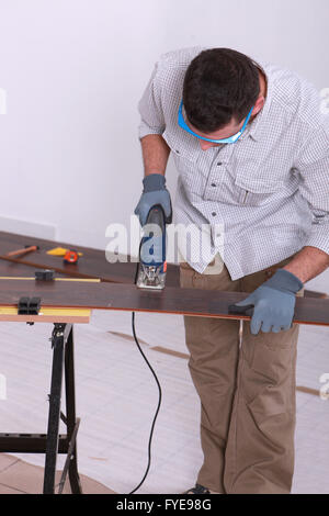 Man using an electric jigsaw to cut a piece of wooden flooring Stock Photo