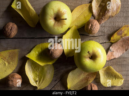 Close up photo of two yellow apples, walnuts and autumn leaves on wood Stock Photo