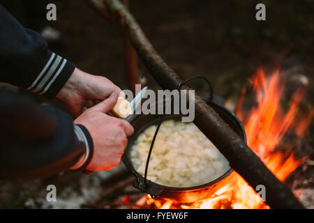 Fish soup cooking on fire in nature and the human hands cut potatoes in a pan. Stock Photo