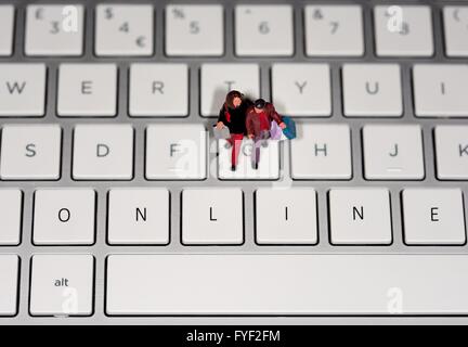 A miniature figurine couple carrying shopping bags on a laptop keyboard with the word ONLINE digitally edited onto the keys. Stock Photo