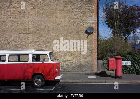 A parked red VW camper van parked next to a faded red Royal Mail postal box on a residential street in Herne Hill, London SE24. Stock Photo