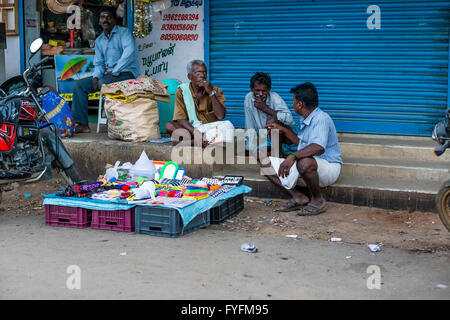 Three men sitting on steps trying to sell goods at the side of the Chennai Road, Villupuram, Tamil Nadu, India Stock Photo