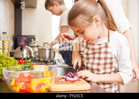 Family cooking background. Happy teen girl cutting onion on chopping board. Stock Photo